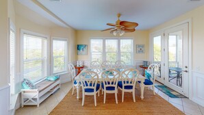A dining area with a white table and chairs, large windows, and a ceiling fan.