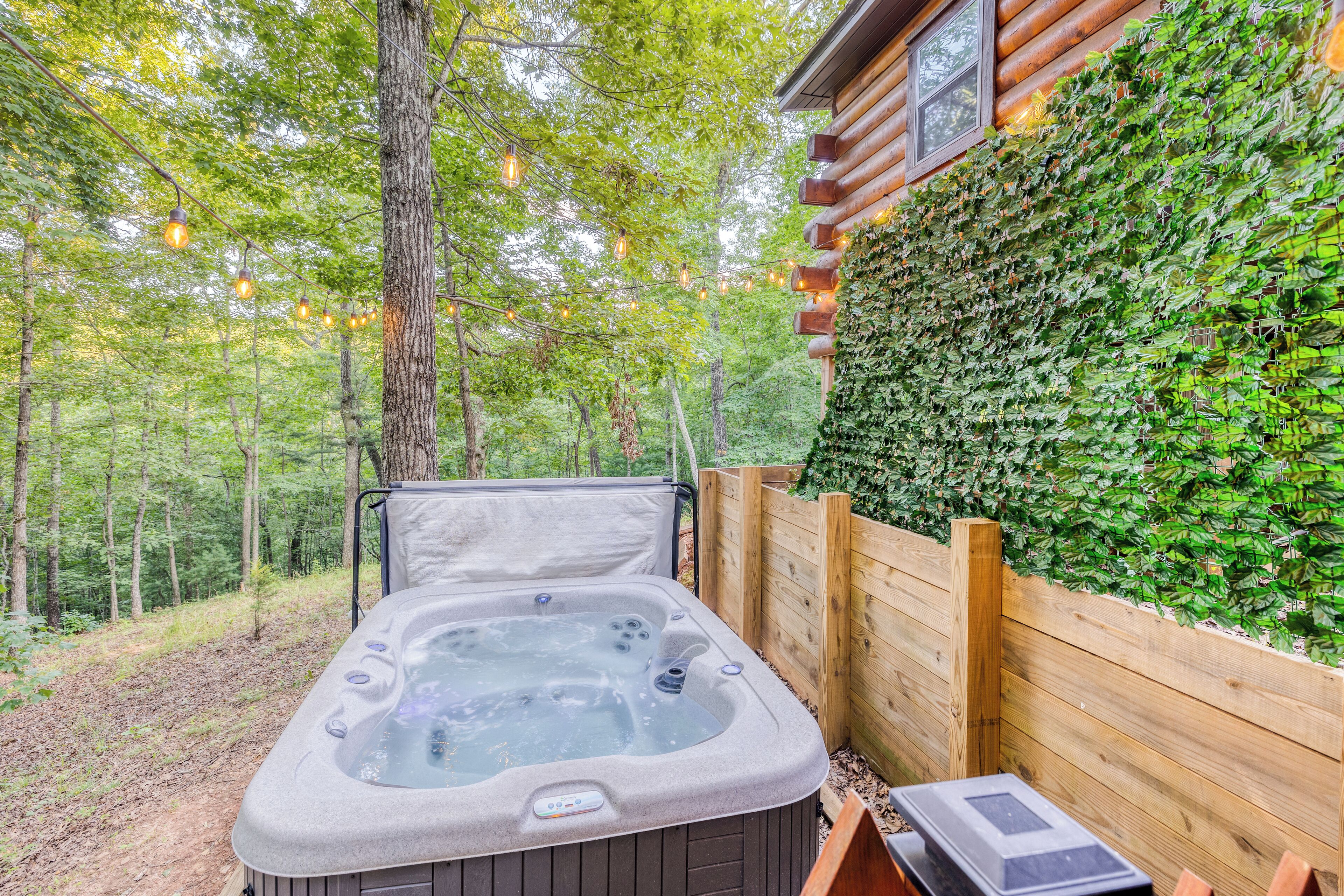 Un jacuzzi en zona boscosa, con una terraza de madera y una pared cubierta de hiedra.