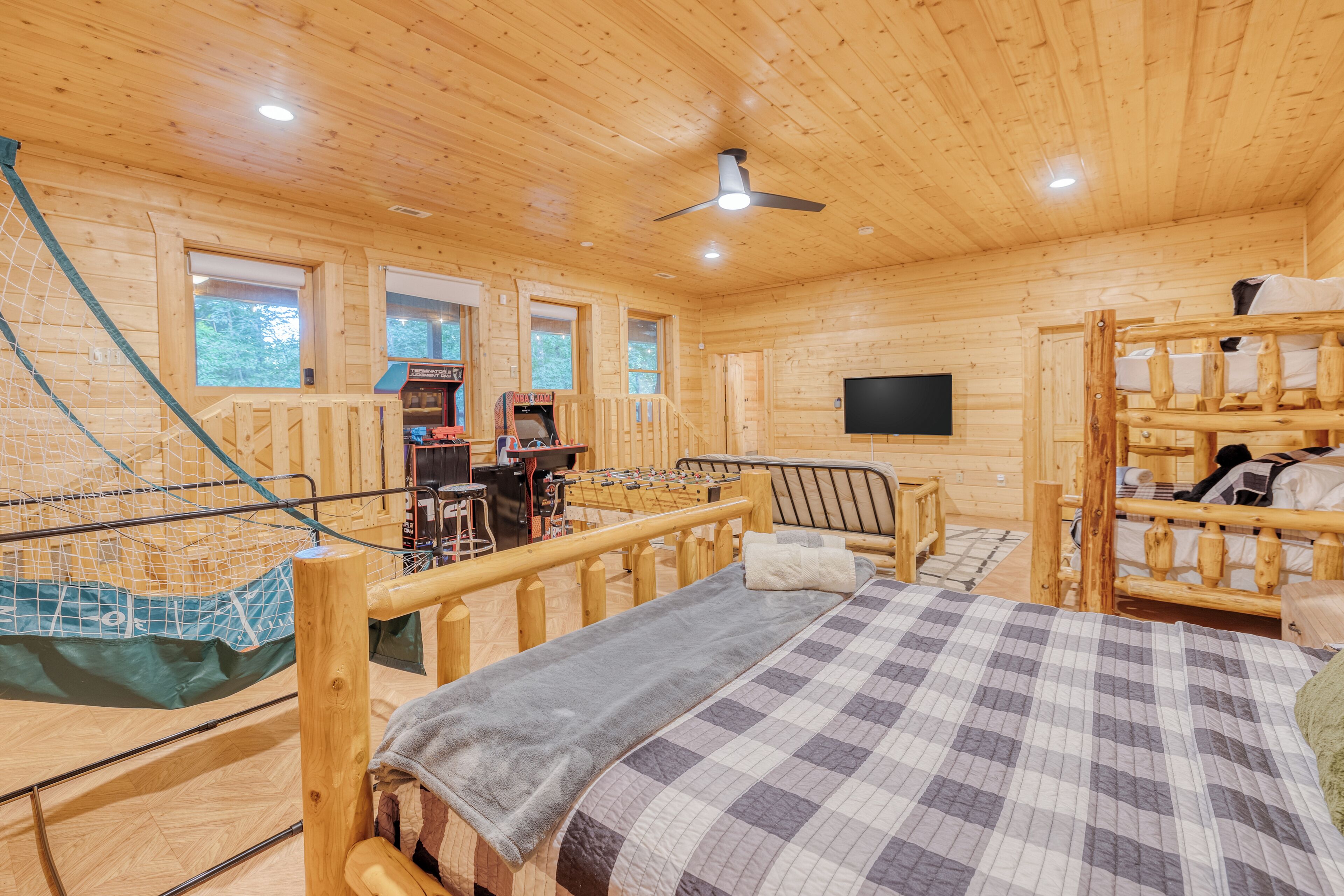 A wooden cabin interior with a bunk bed, a desk with a computer, and a television mounted on the wall.