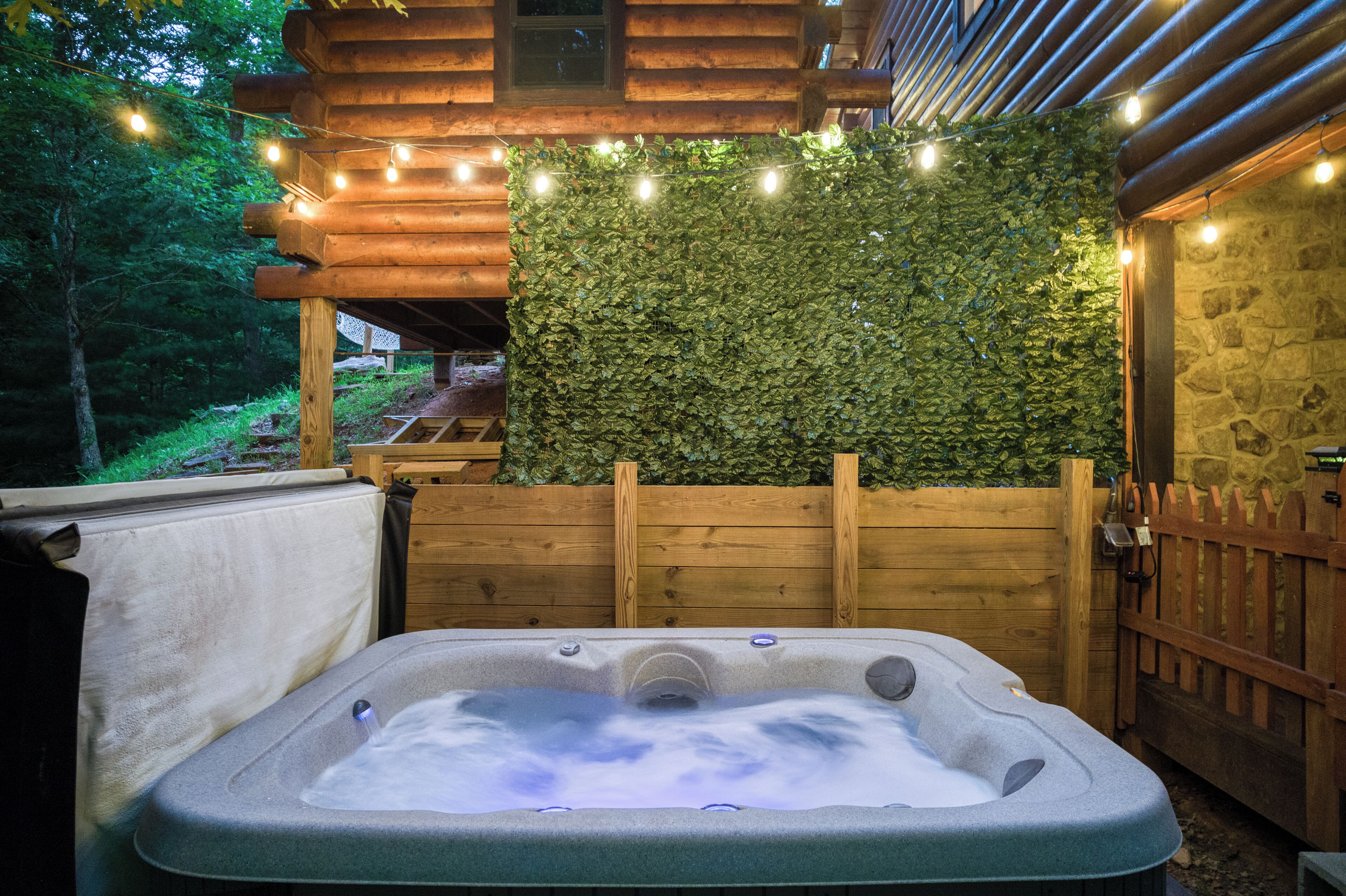 A hot tub with a wooden deck and a wall covered in foliage, surrounded by a wooden fence and stone walls.