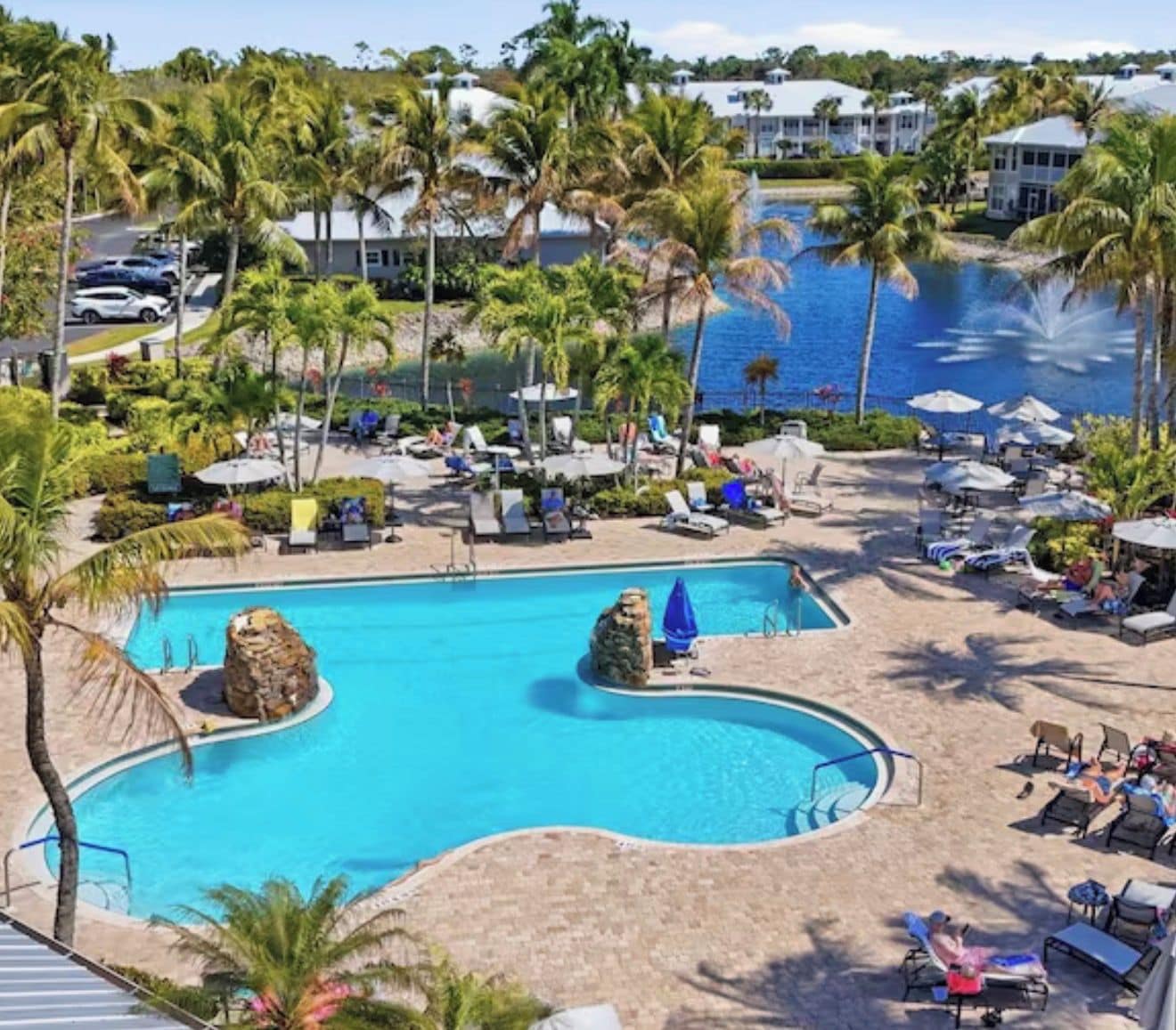 A resort pool with palm trees, lounge chairs, and a view of the ocean.
