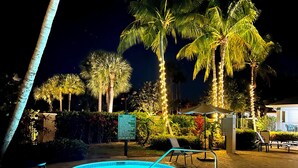 Ein Poolbereich bei Nacht mit Whirlpool, Palmen und einem Schild, das eine maximale Spa-Tiefe von 36 Zoll angibt.