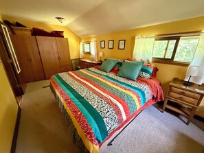 A bedroom with a large bed, wooden wardrobe, bedside table, and a window with curtains.