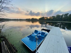 A calm lake with a wooden dock and a blue paddle boat.