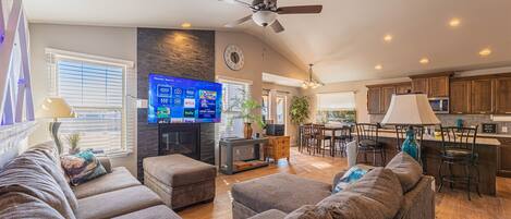 A spacious living room with a large flat-screen TV, comfortable seating, and a ceiling fan.