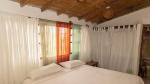 Un dormitori amb llit, cortines, un panell de capçalera de fusta i un ventilador de sostre.