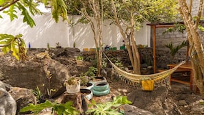 Un jardí rústic amb cadira d'hamaca, pedres i plantes en testos.