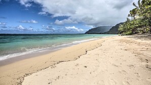 A beach with clear turquoise water, a sandy shore, and a backdrop of lush green hills. - WFH in Paradise: Beachfront Hauula Getaway! (Hauula)