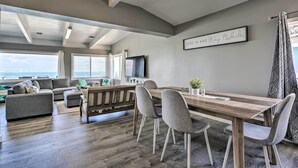 A spacious living area with a wooden dining table, grey upholstered chairs, a grey sofa, and a television on the wall. - WFH in Paradise: Beachfront Hauula Getaway! (Hauula)