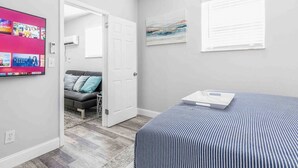 A bedroom with a bed, a grey sofa, a TV on the wall, and a window. - Kick back and relax in this calm, stylish space (Fort Lauderdale)