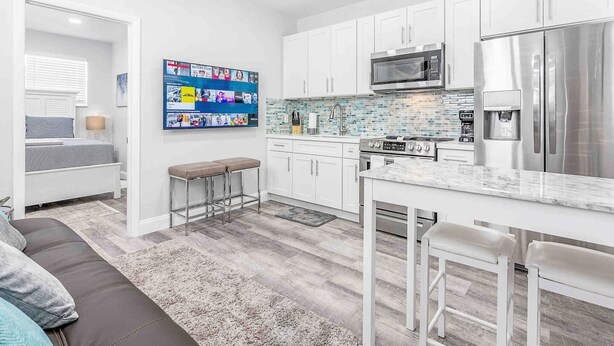 A modern kitchen with white cabinets, stainless steel appliances, a tiled backsplash, and a bar area with stools. - Kick back and relax in this calm, stylish space (Fort Lauderdale)