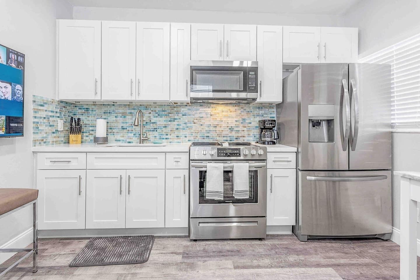 Una cocina moderna con armarios blancos, un refrigerador de acero inoxidable, un microondas y un horno.