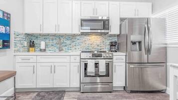 Una cocina moderna con armarios blancos, un refrigerador de acero inoxidable, un microondas y un horno.