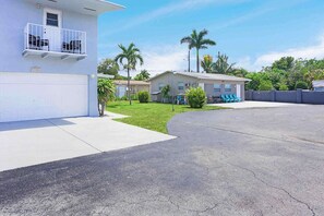 A residential street with houses, a garage, and a grassy area with palm trees.