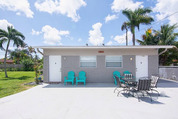 A two-story building with numbered doors, outdoor seating, and palm trees.