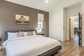 Een slaapkamer met een groot bed, een nachtkastje, een wandlamp en een raam met jaloezieën.