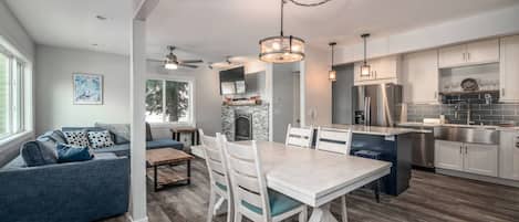A modern kitchen with white cabinetry, a dining area with a white table and chairs, and a gray sofa with blue cushions.