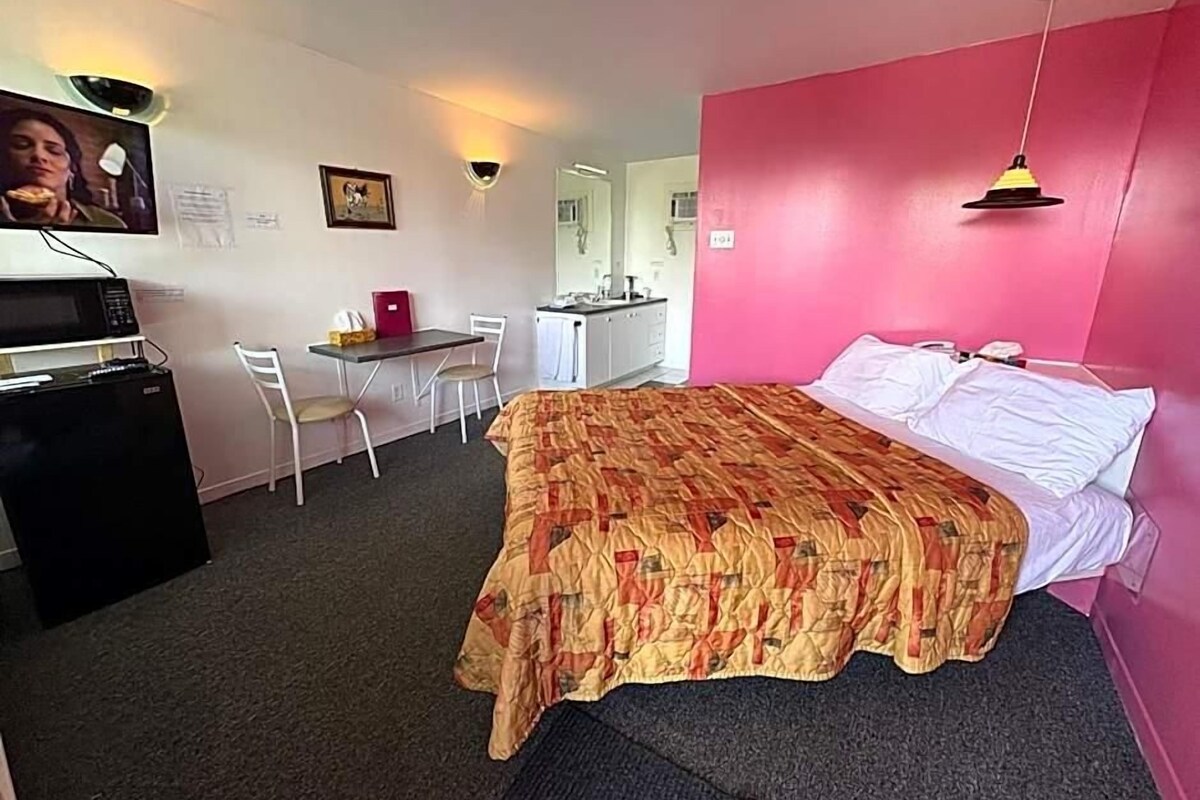 A bedroom with a bed, a desk, a chair, a microwave, and a refrigerator.
