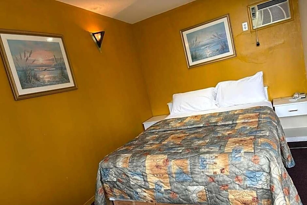A room with a bed, two framed pictures on the walls, a bedside table, and a wall-mounted air conditioning unit.