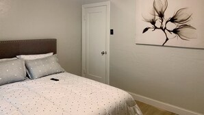 Un dormitorio con cama, almohadas, un cuadro, un ventilador de techo y una puerta.