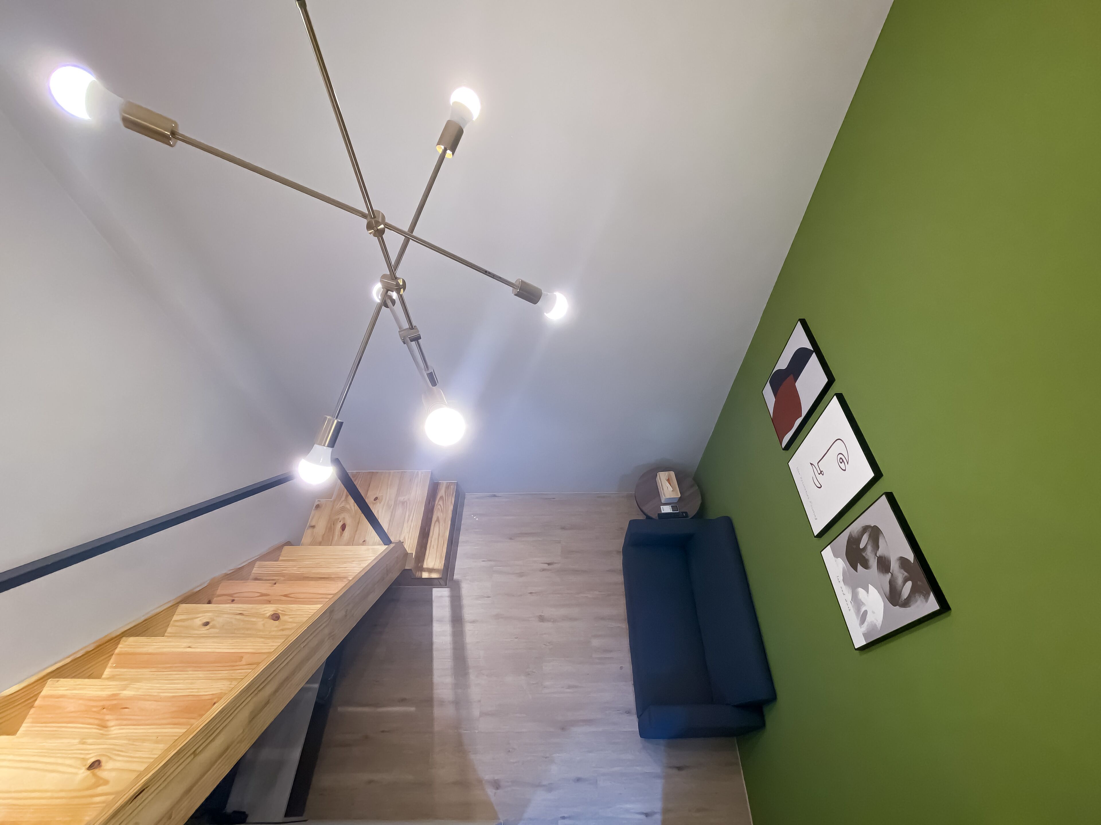 A modern interior with a wooden staircase, a green accent wall, and a ceiling light fixture.