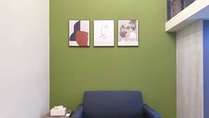 Een kamer met een groene wand, een blauwe bank en drie kunstwerken in lijsten.