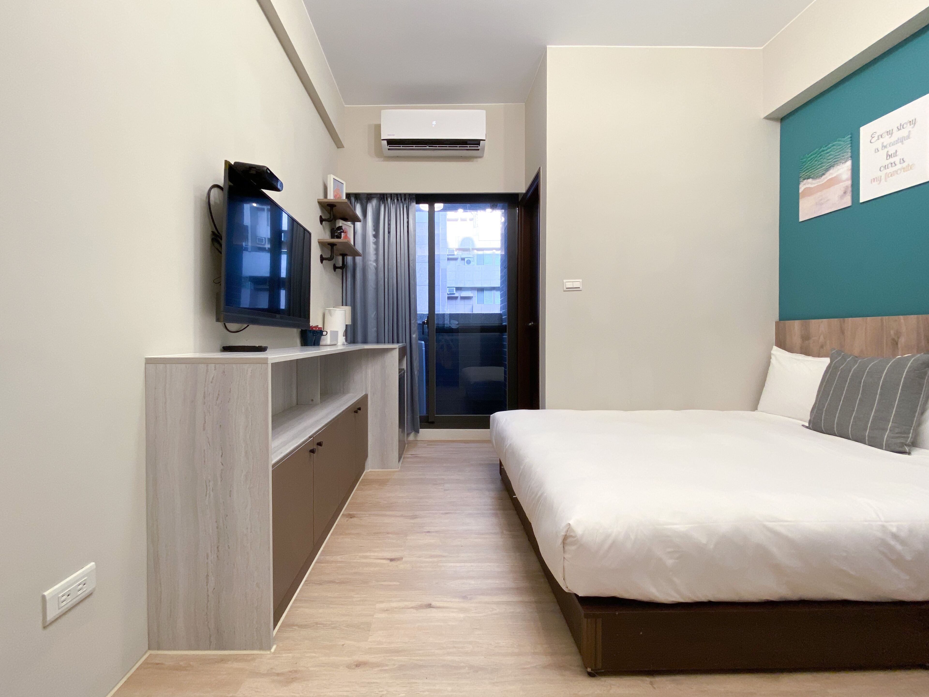 A hotel room with a bed, a TV, a desk, and a view of the outside.
