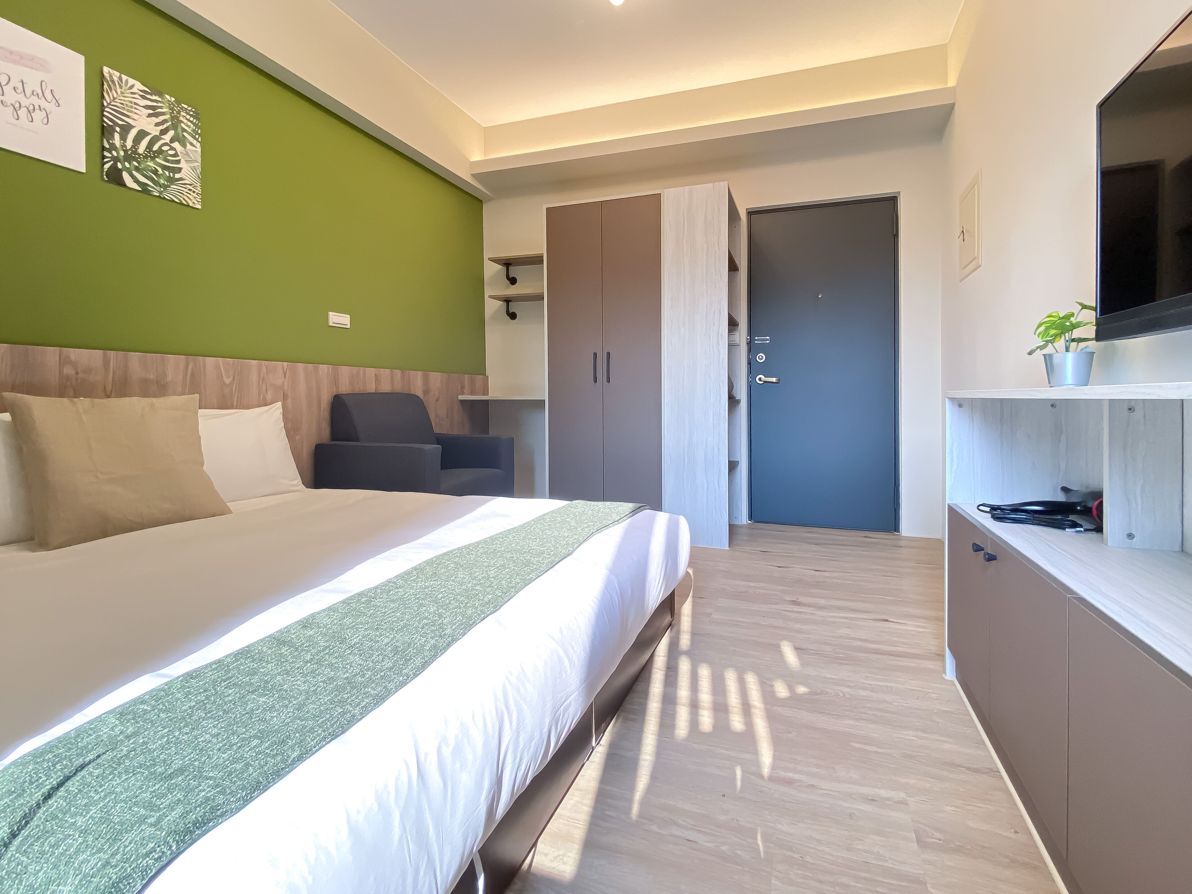 A modern hotel room with a large bed, a desk, a chair, and a wardrobe.