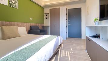 A modern hotel room with a large bed, a desk, a chair, and a wardrobe.