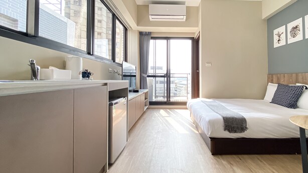Een moderne hotelkamer met een kitchenette, een groot bed, een kleine tafel en een balkon met uitzicht over de stad.