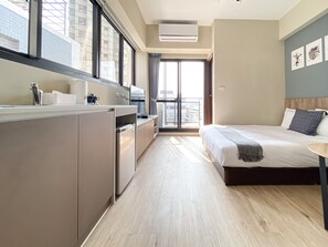 Una habitación de hotel moderna con kitchenette, una cama grande, una mesita y un balcón con vista a la ciudad.