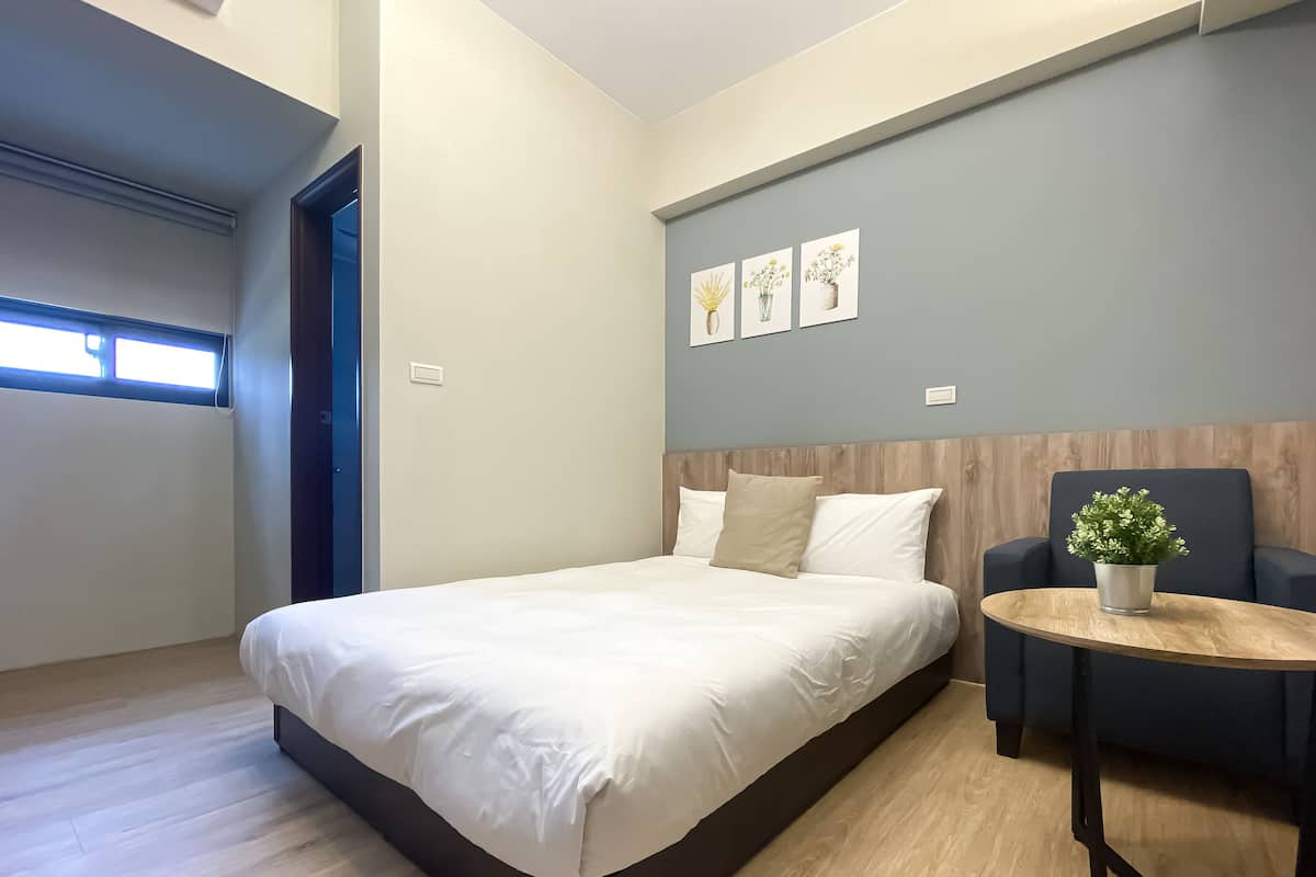 A modern bedroom with a large bed, a small round table with a plant, and three wall-mounted artworks.