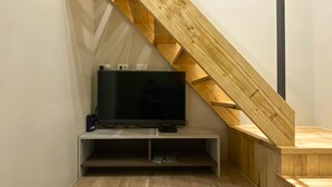 Een moderne kamer met een houten trap, een flatscreen televisie op een witte standaard, en een houten vloer.