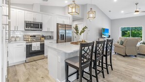 Una cocina moderna con armarios blancos, electrodomésticos de acero inoxidable y una isla central con taburetes de bar.