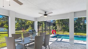 Un patio exterior con una mesa y sillas de comedor, un ventilador de techo y vistas a una piscina y zonas verdes.