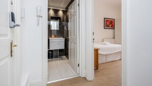 Una habitación de hotel moderna con una puerta blanca, un baño con espejo, lavamanos e inodoro, y una cama con edredón blanco.