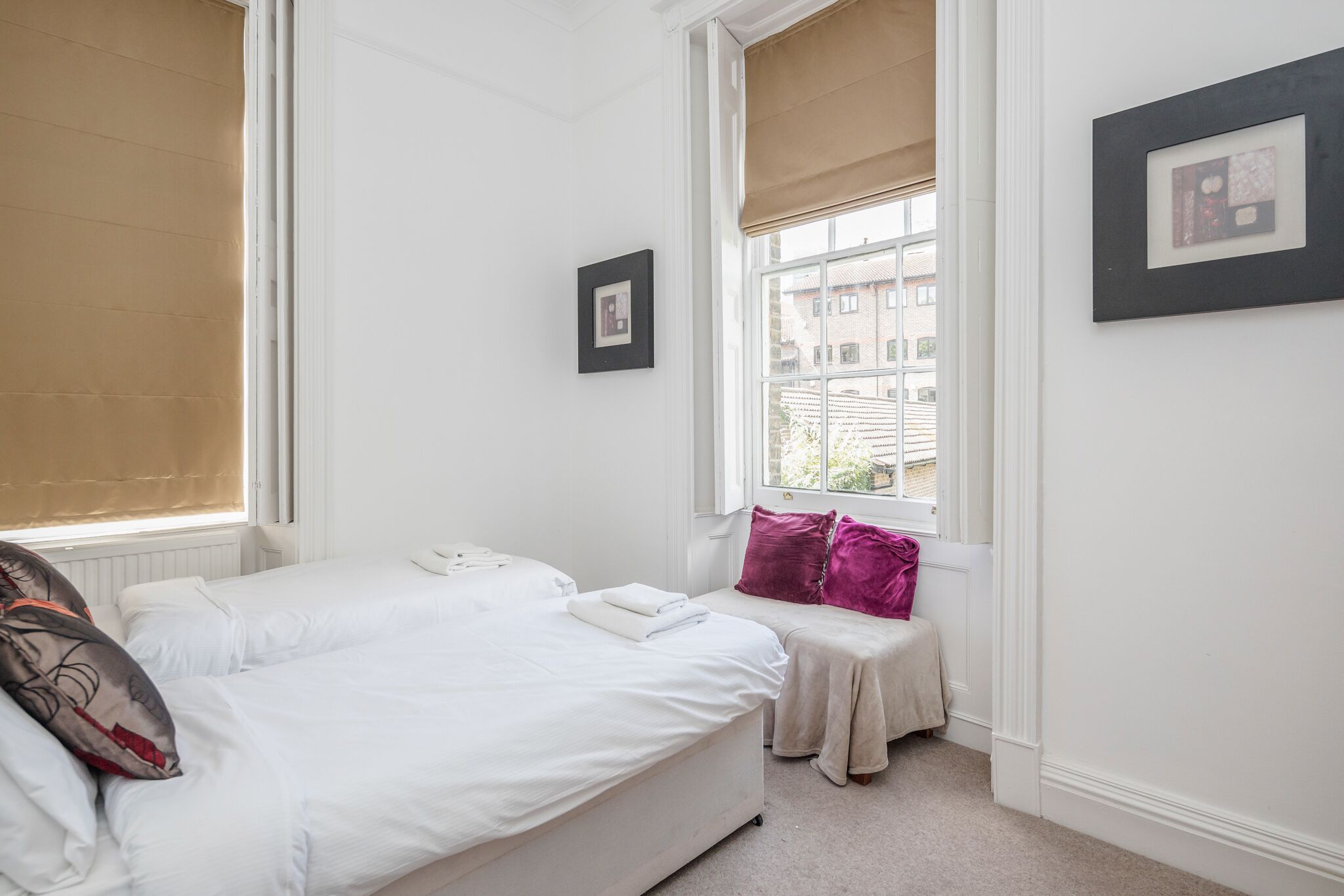 A hotel room with two beds, a window with a view, and a framed picture on the wall.