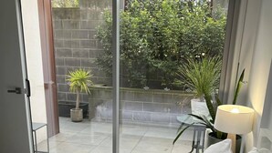 Quarto com uma grande porta de vidro deslizante que dá para um alpendre com vasos de plantas e uma parede de tijolos.