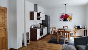 A modern kitchen with white cabinets, a stainless steel refrigerator, and a dining area with wooden chairs and a table.