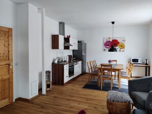 A modern kitchen with white cabinets, a stainless steel refrigerator, and a dining area with wooden chairs and a table. - Vacation apartment Krottenmühl am Simssee, 55 sqm, first floor, 1 separate bedroom (Söchtenau)
