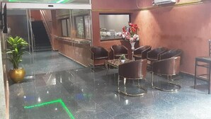 A reception area with a glass partition, a reception desk, several chairs, a table with a vase of flowers, and a potted plant. - Royal City Dubai Hotel & Suites (Nkpor)