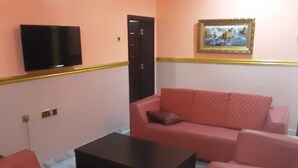 A room with a red sofa set, a black coffee table, a flat-screen TV mounted on the wall, and a door with a golden frame. - Royal City Dubai Hotel & Suites (Nkpor)