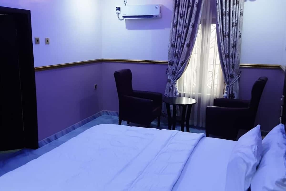 Une chambre d’hôtel avec un lit, deux chaises, une petite table et un appareil de climatisation.