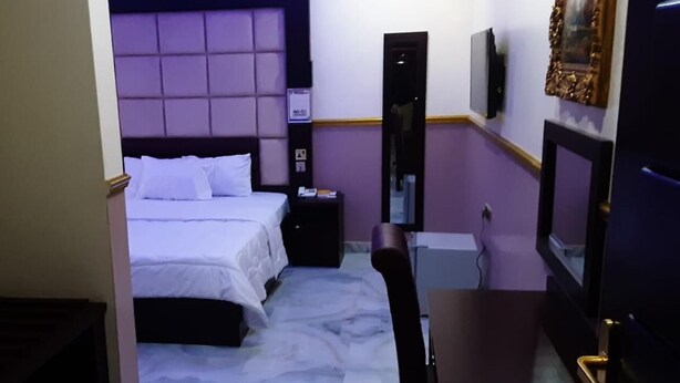 A hotel room with a bed, a desk, a chair, a television, and a mirror. - Royal City Dubai Hotel & Suites (Nkpor)