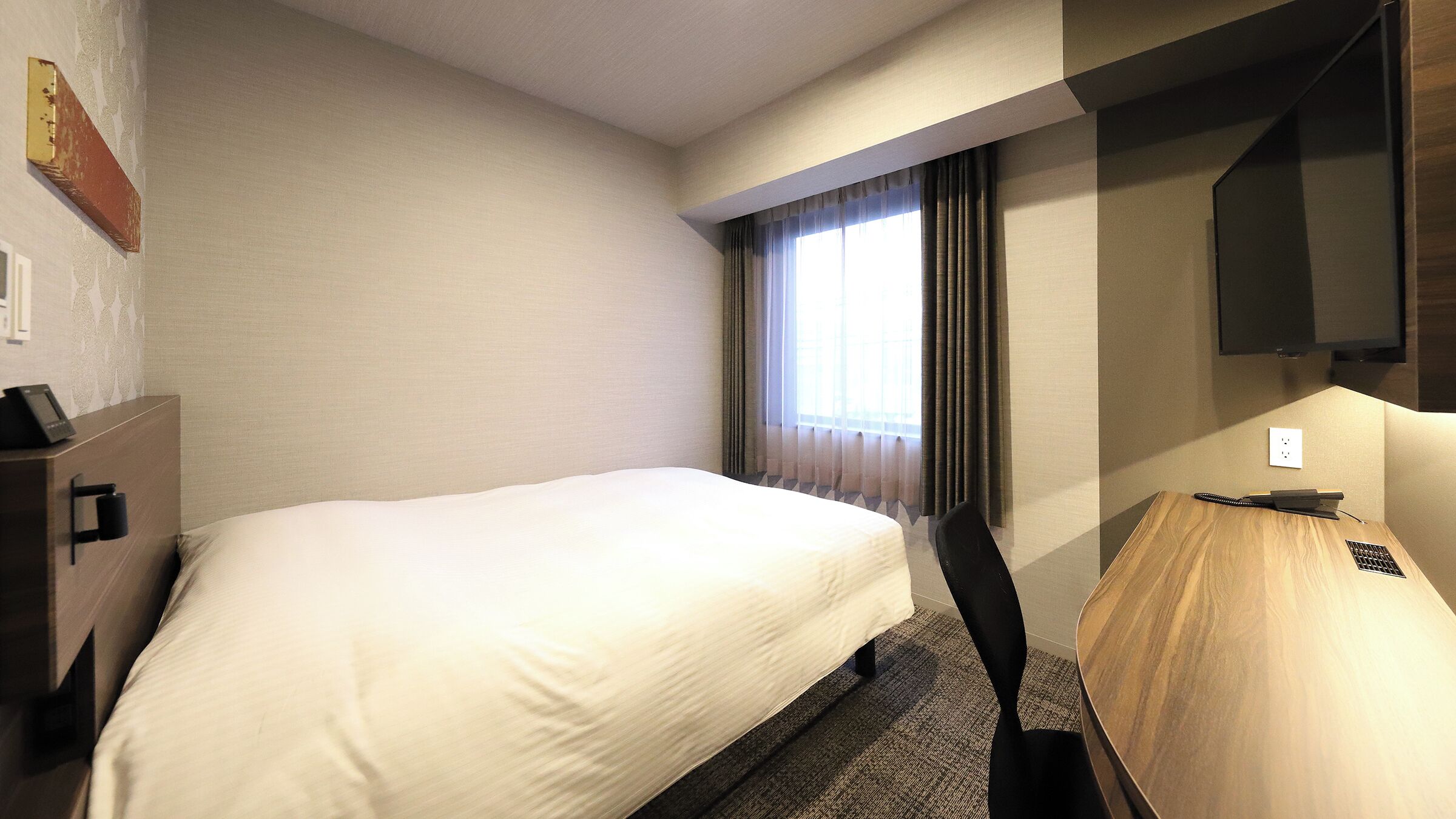 A hotel room with a bed, a desk, a chair, a television, and a window with curtains.