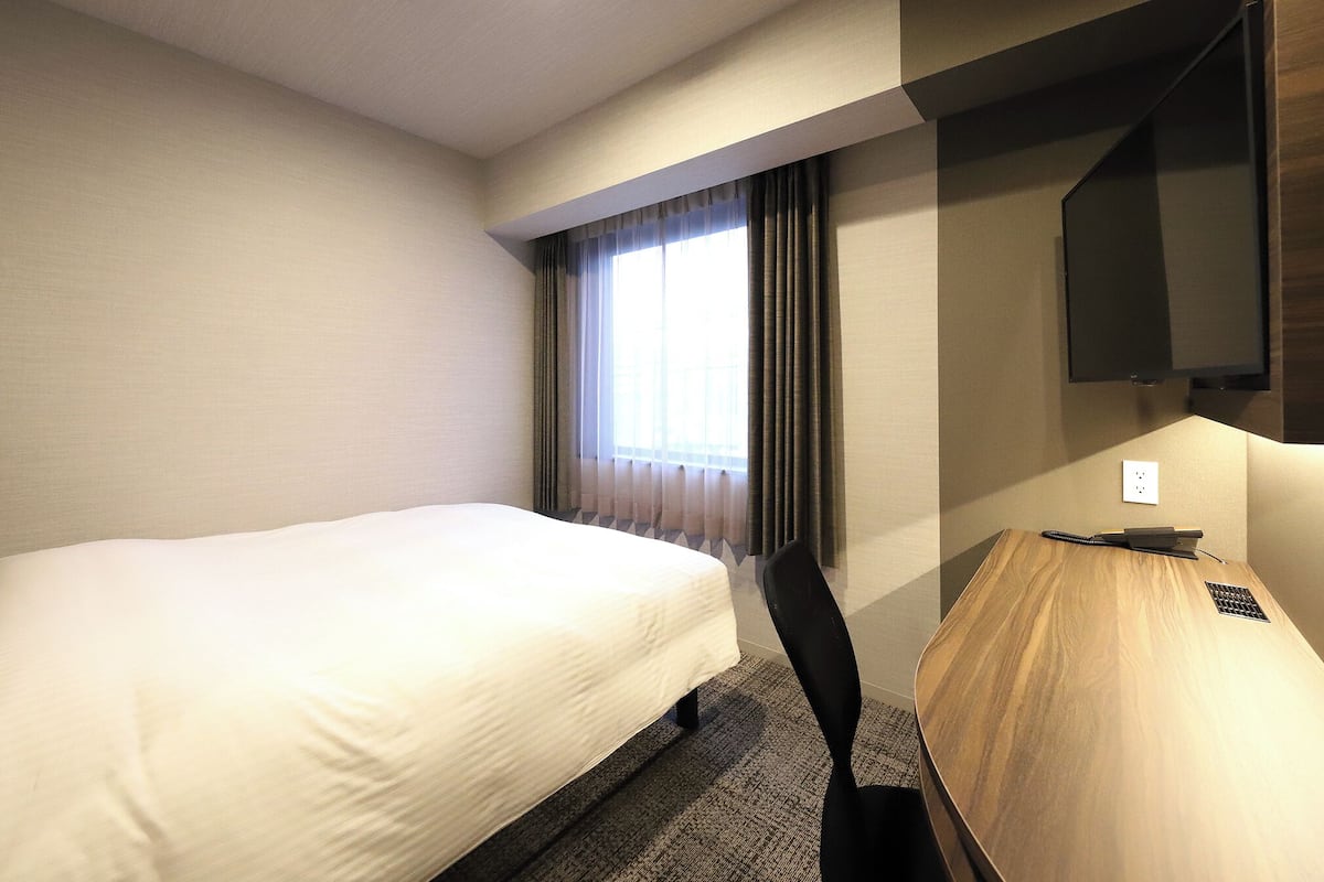 A hotel room with a bed, a desk, a chair, a television, and a window with curtains.