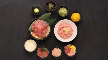 Variedad de platos japoneses, como sashimi, arroz y vegetales encurtidos, sobre una superficie oscura.