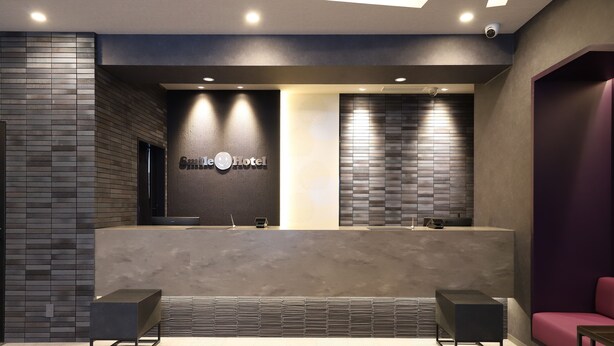 A modern reception area with a dark reception desk, a large mirror, and a seating area with a purple couch. - Smile Hotel Kanazawa Nishiguchi Ekimae (Kanazawa)