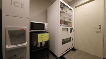 Màquina expenedora amb diverses begudes i aperitius, un microones i un dispensador d'aigua a una habitació d'hotel.