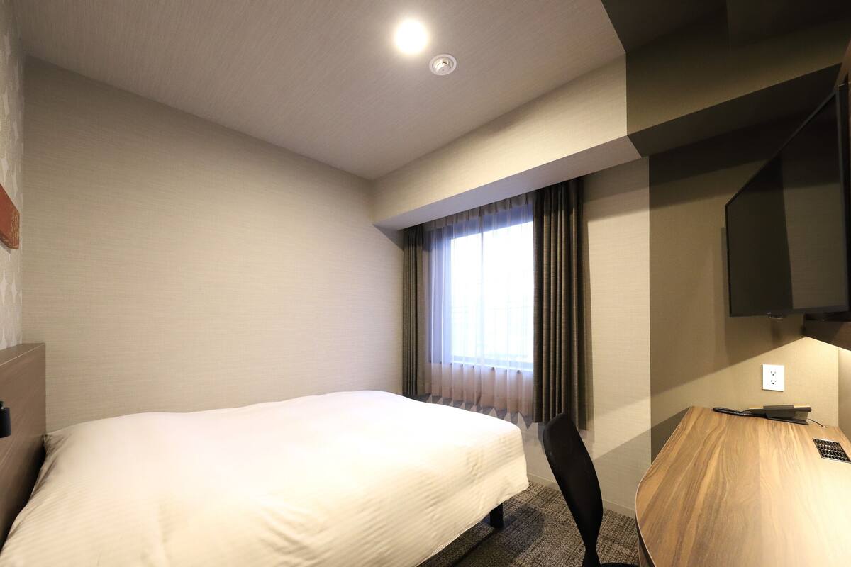 A hotel room with a bed, a desk, a chair, a television, and a window with curtains.